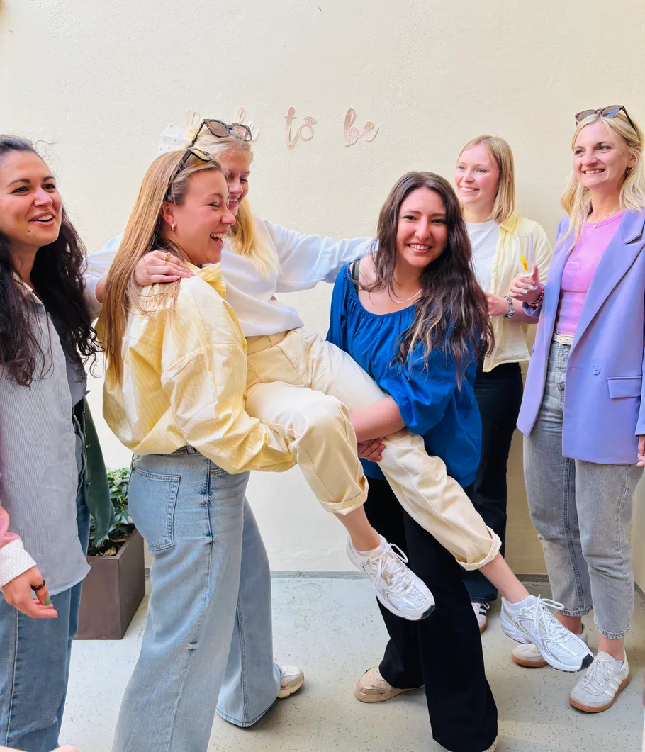 Group of women laughing, lifting another indoors.