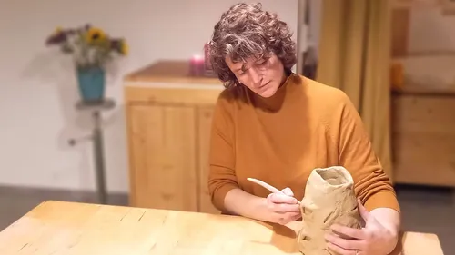 Person sculpting clay on wooden table indoors.
