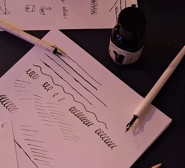 Kalligraphieübung mit Tinte und Stiften auf Papier.