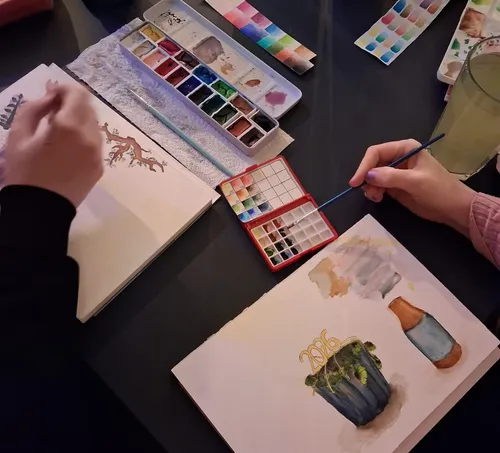 Zwei Personen malen Aquarelle an einem Tisch.