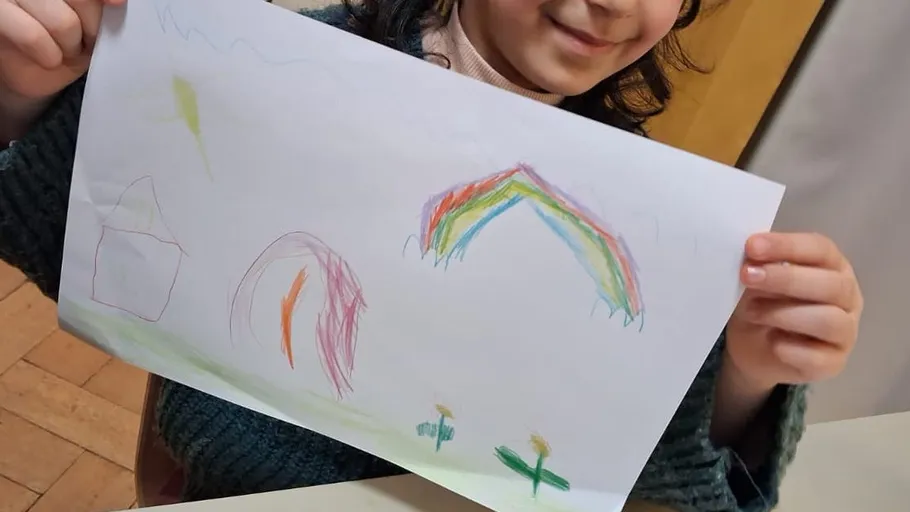Child holding drawing with rainbow and house.