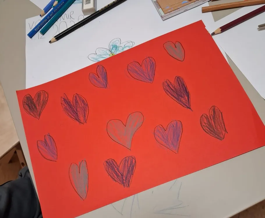 Bunte Herzen auf rotem Papier, Bleistifte daneben.