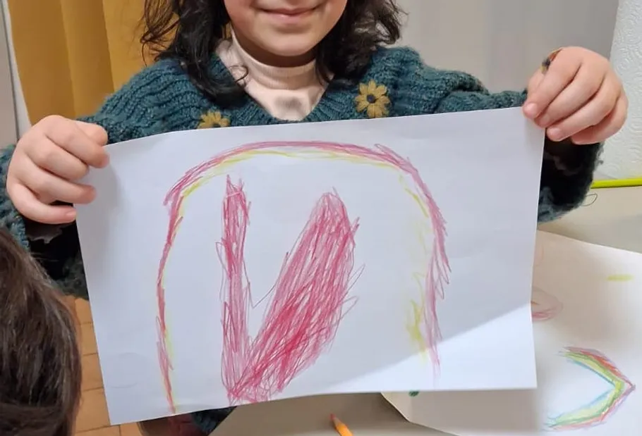 Kind hält Zeichnung mit Rot- und Gelbtönen.