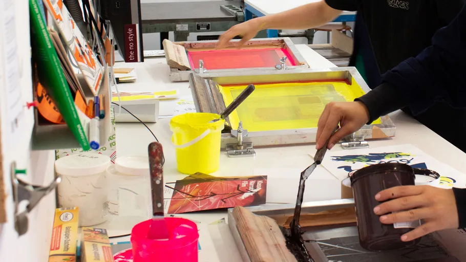 People screen printing at a workshop table.