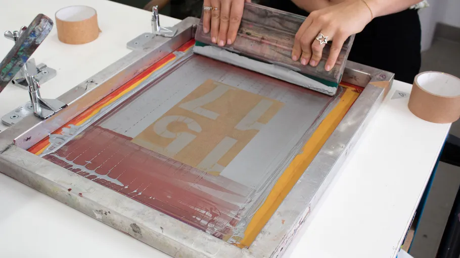 Hands screen printing on a mesh frame.