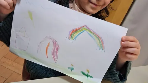 Child holding drawing with rainbow and house.