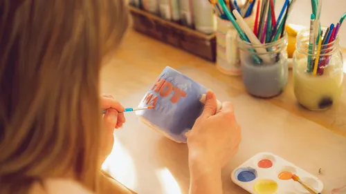 Person painting a mug with brushes nearby.