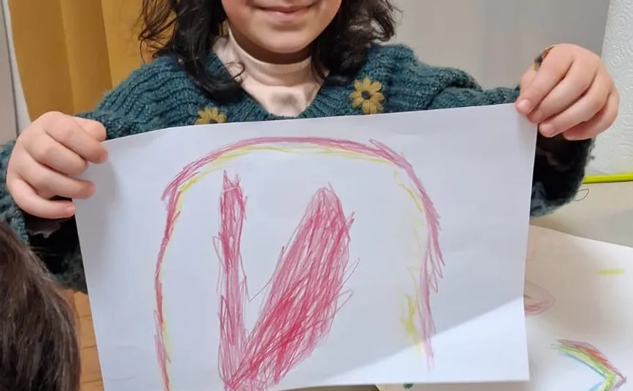 Child holding drawing, smiling indoors.
