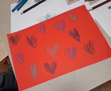 Rotes Papier mit gezeichneten Herzen, Stifte in Nähe.