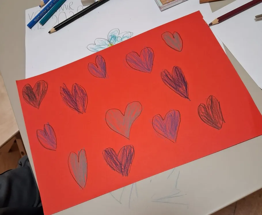 Rotes Papier mit gezeichneten Herzen, Stifte in Nähe.