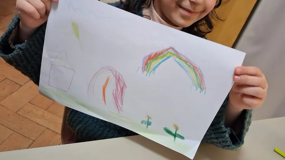Child holding drawing with rainbow and house.