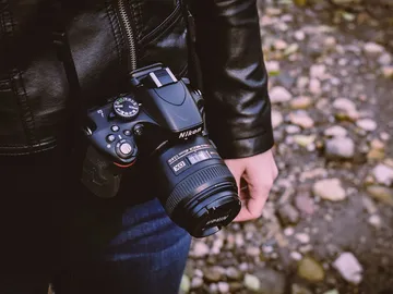 Camera hangs on the wrist, surrounded by rocks and soil.