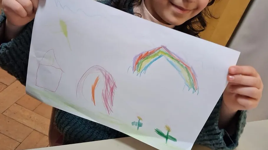 Child holding colorful drawing with rainbow.