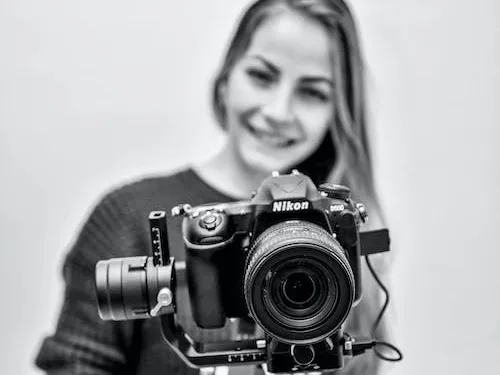 Woman holding camera smiling against a neutral background.