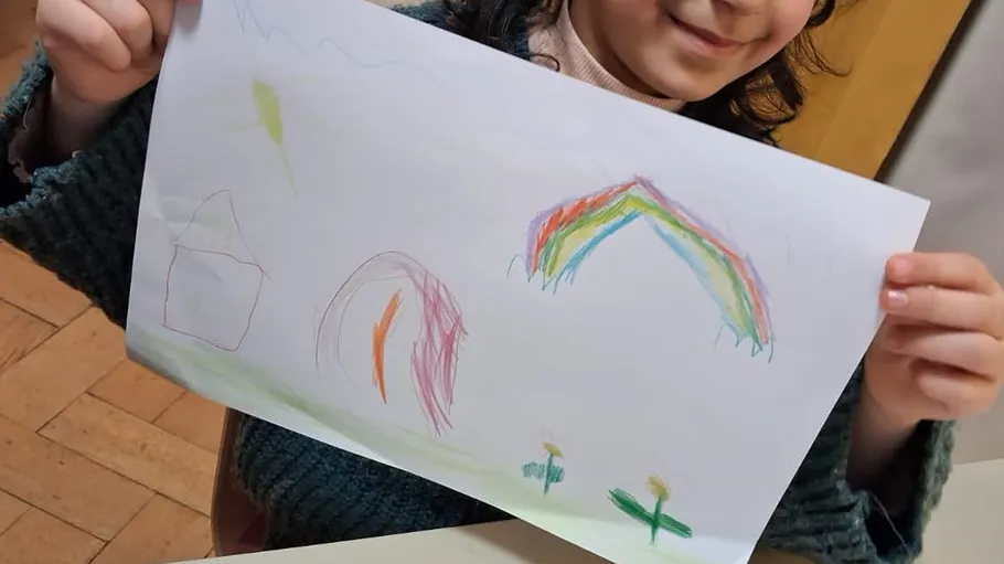 Child holds colorful drawing with rainbow.