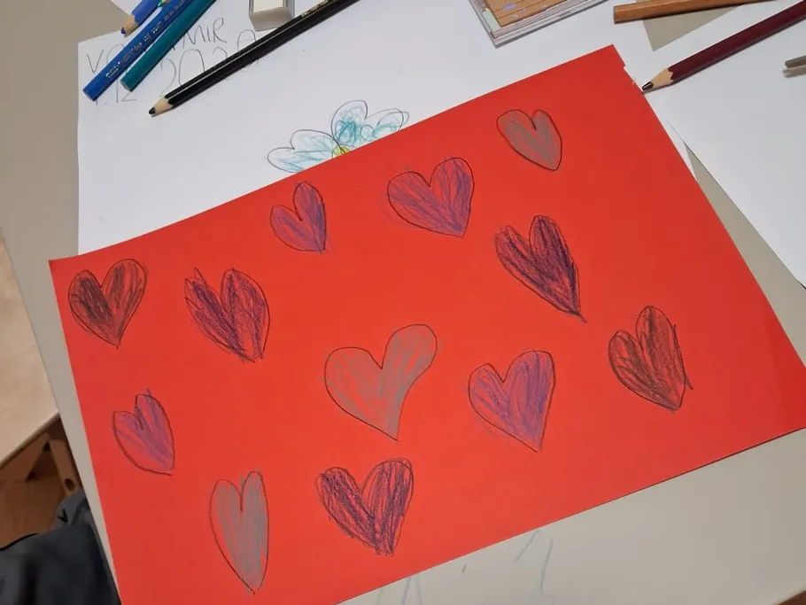 Red paper with hand-drawn hearts on table.