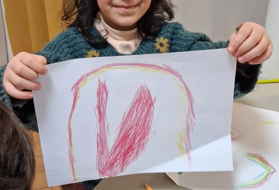 Child holding colorful drawing, smiling indoors.