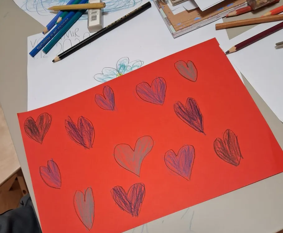 Red paper with hand-drawn hearts on table.