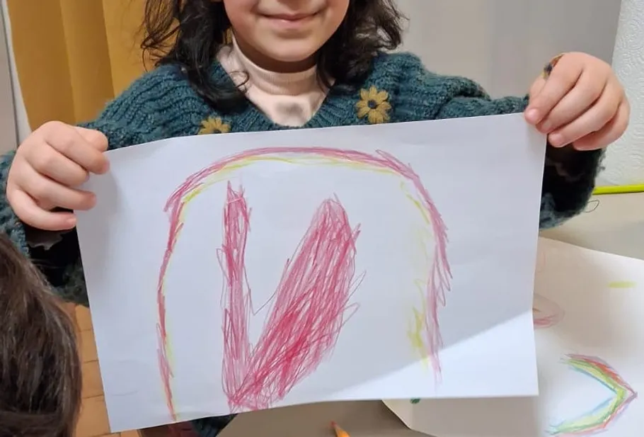 Child holding colorful drawing indoors.
