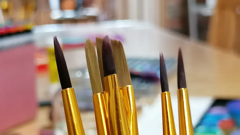 Painting brushes with gold handles on a desk.