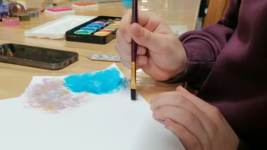 Person malt auf Papier mit Aquarellpalette.