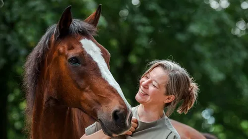 Woman smiling beside a brown horse outdoors.