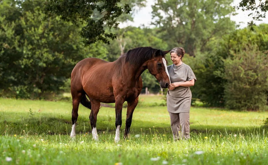 Woman walking with horse in grassy field.