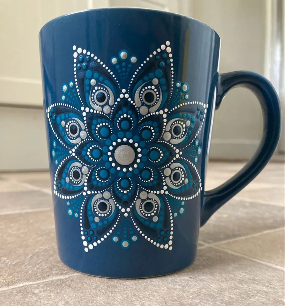 Blue mug with mandala design on tiled floor.