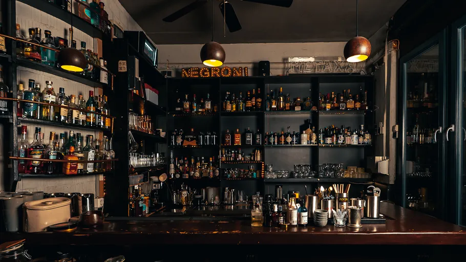 Schummrig beleuchtete Bar mit Regalen voller Flaschen.