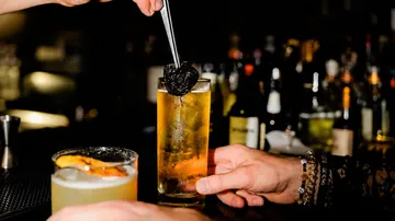 Bartender placing garnish in cocktail glass.