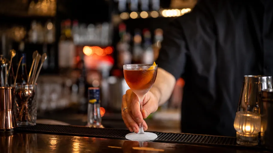 Bartender serves cocktail on bar counter.