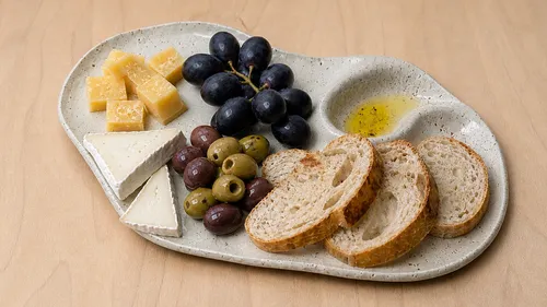 Käse, Trauben und Brot auf Keramikplatte.