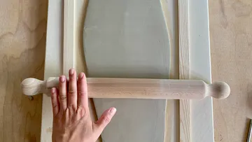 Hand holds rolling pin over dough frame.