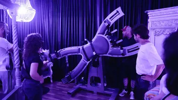 People observing a large mechanical chair in a room.