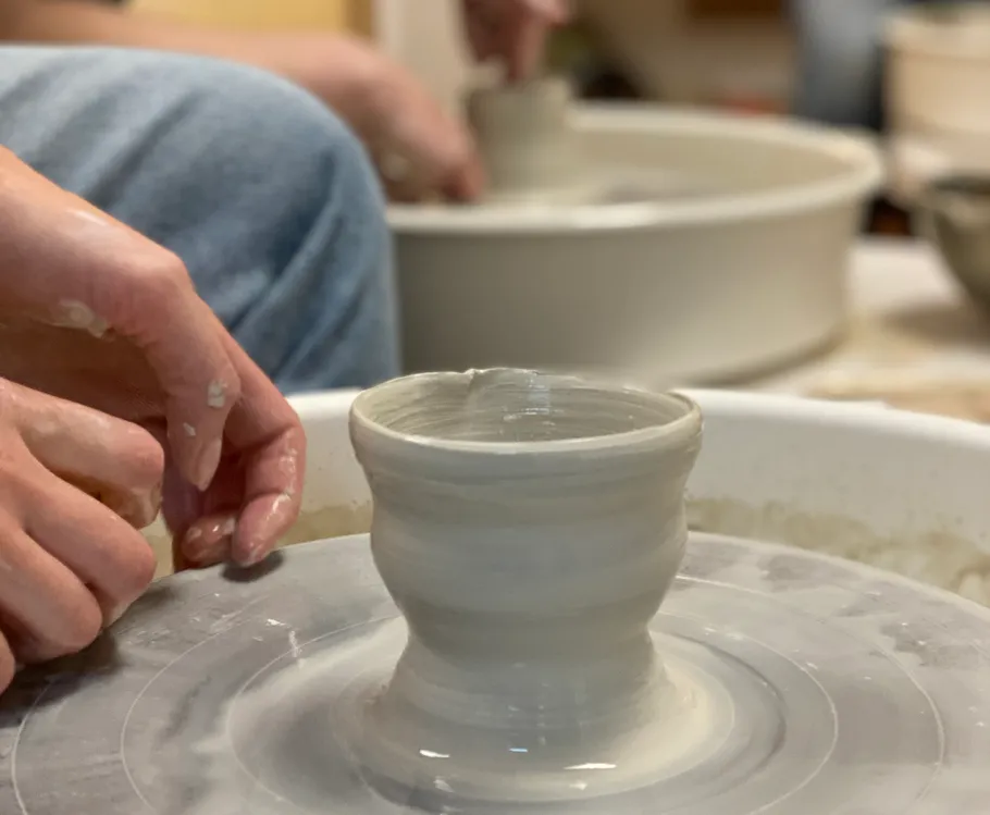 Hands shaping clay on pottery wheel, indoor setting.