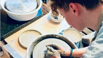 Person shaping clay on pottery wheel indoors.