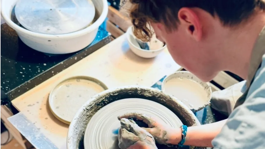 Person shaping clay on pottery wheel indoors.