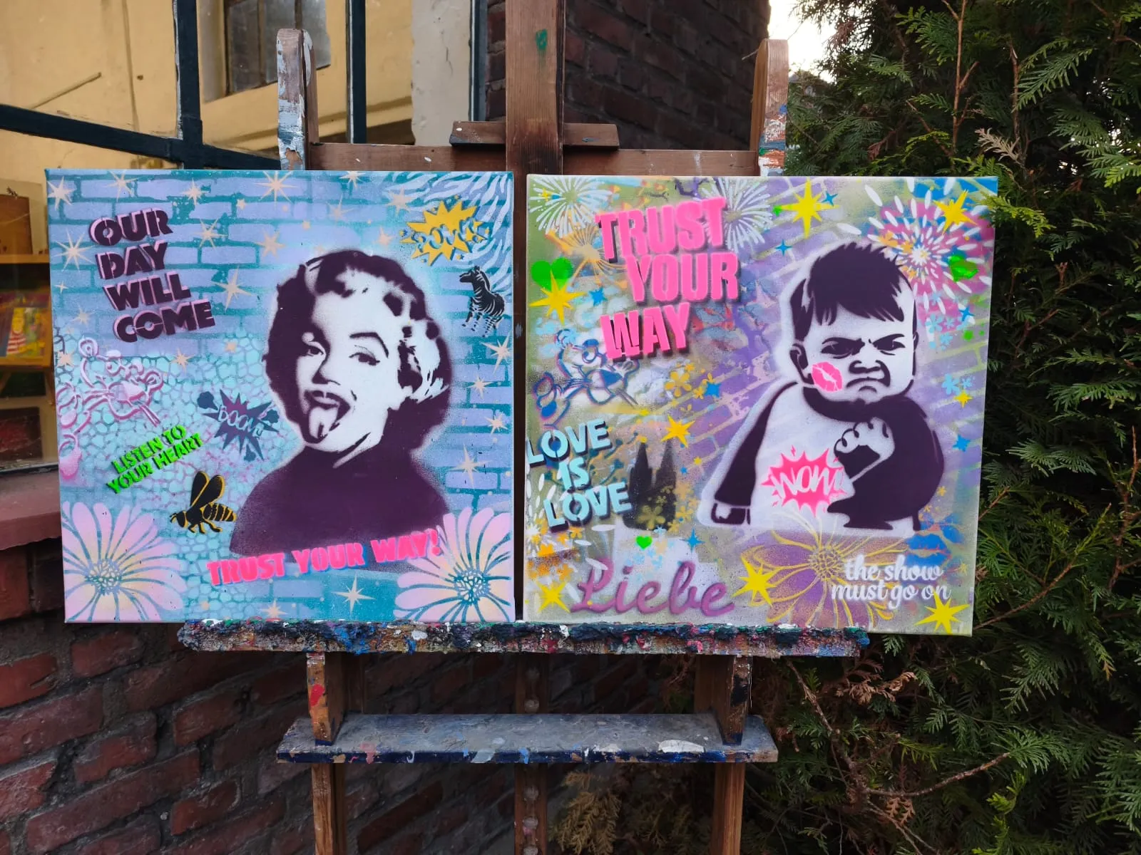 Zwei Schablonen-Kunstwerke auf Staffelei draußen.