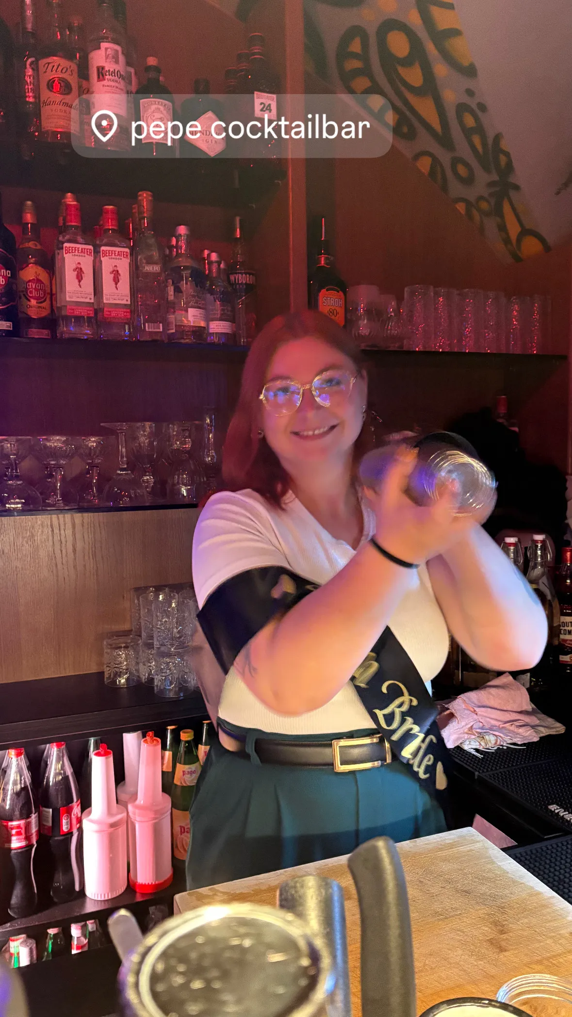 Person schüttelt Cocktailshaker hinter Bar.