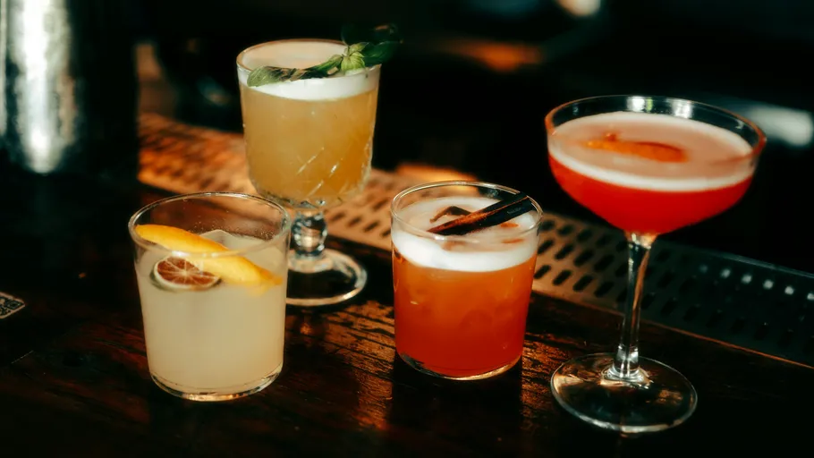 Vier bunte Cocktails auf einer Holzbar.