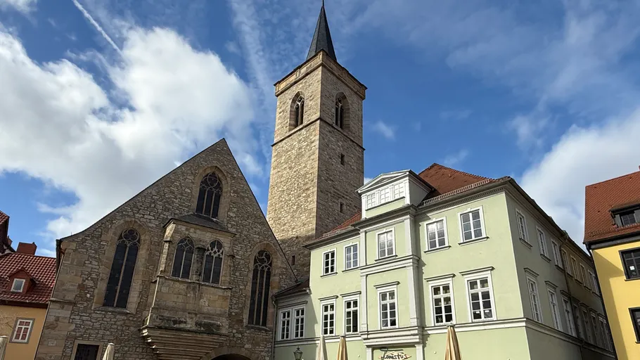 Historisches Gebäude und Kirchturm unter blauem Himmel.