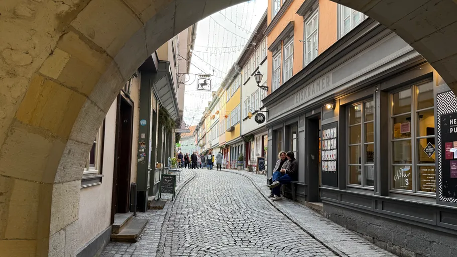 Cobblestone street viewed through archway, people walking.