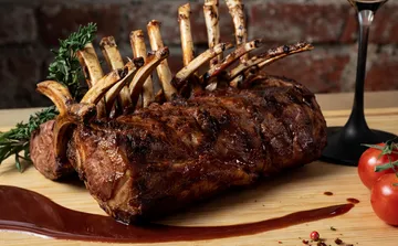 Roasted lamb rack with sauce on wooden board.