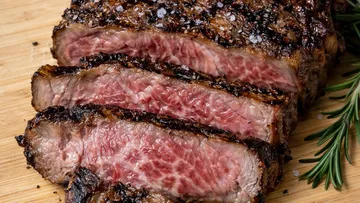Sliced steak with salt on wooden board.