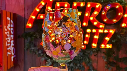 Verziertes Aperol-Glas gehalten, leuchtendes Schild im Hintergrund.