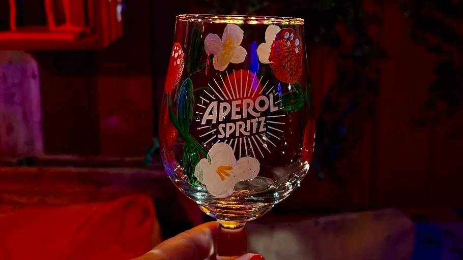 Hand hält Glas mit gemalten Blumen drinnen.