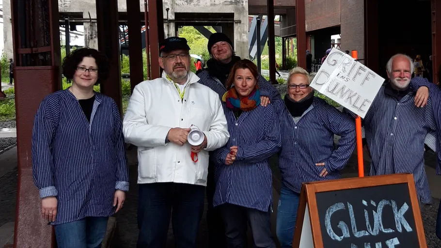 Group posing in striped shirts with a sign.