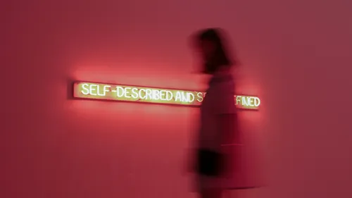 Verschwommene Person passiert Neonkunst an Wand.