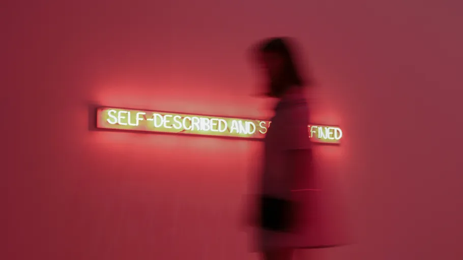Blurry figure passes neon art on wall.