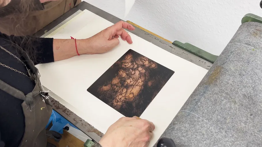 Person untersucht Kunstwerk auf Druckerpresse.